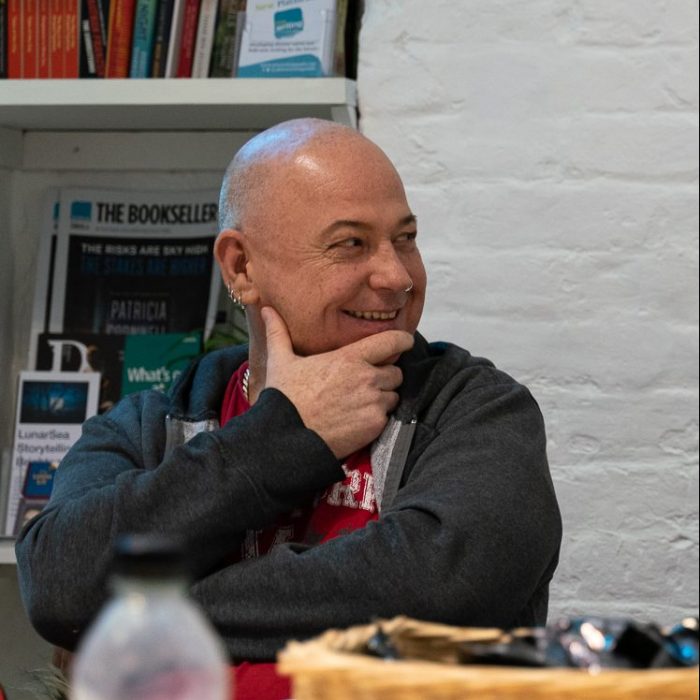 A participant with a bald head is smiling at something off camera. They are resting their head on their hand.