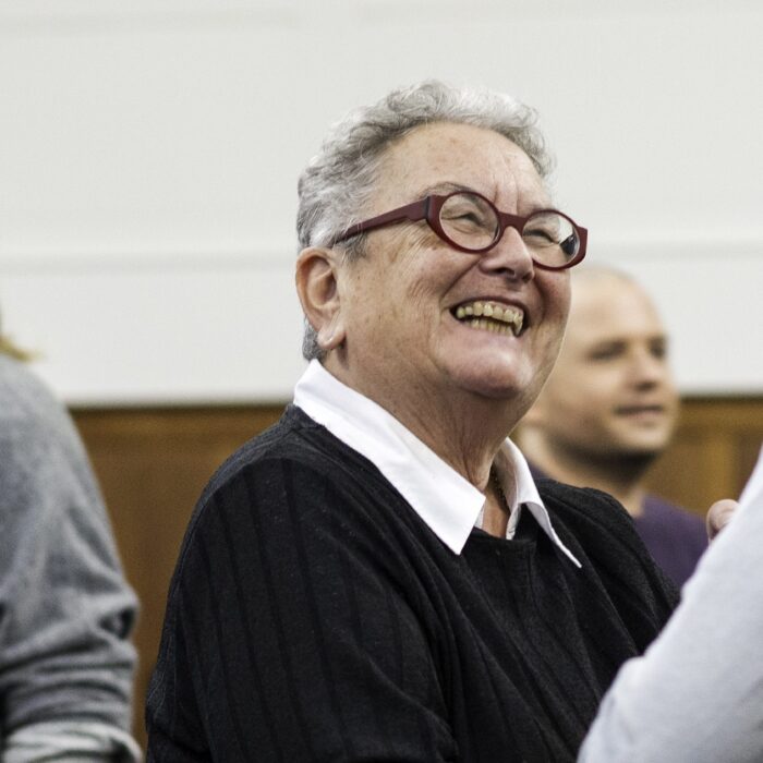 A group of people are stood interacting in a workshop focusing on one participant smiling at another.