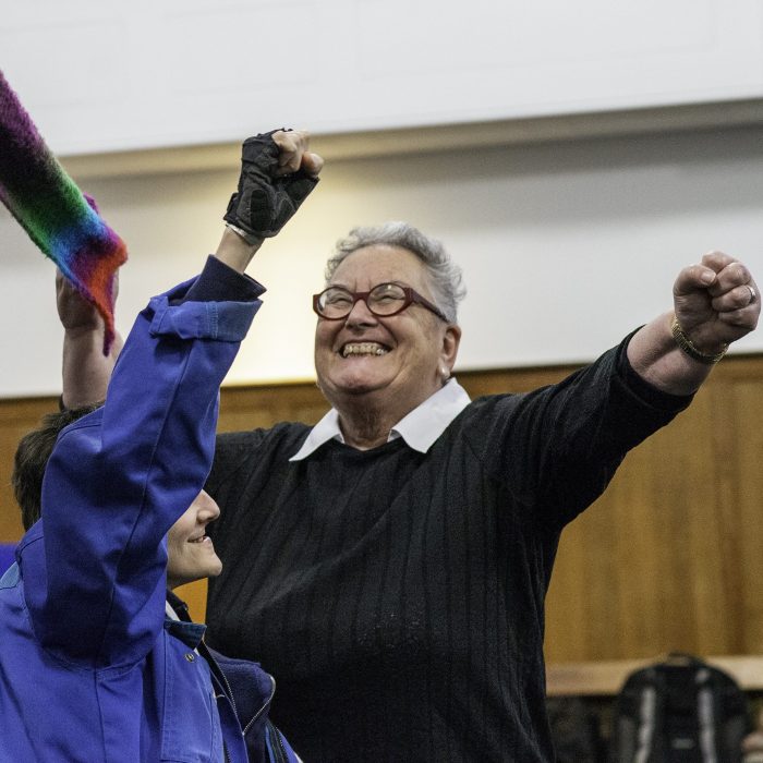 A performance with 2 people. They are smiling and have their firsts in the air holding a scarf as if it was a protest banner.