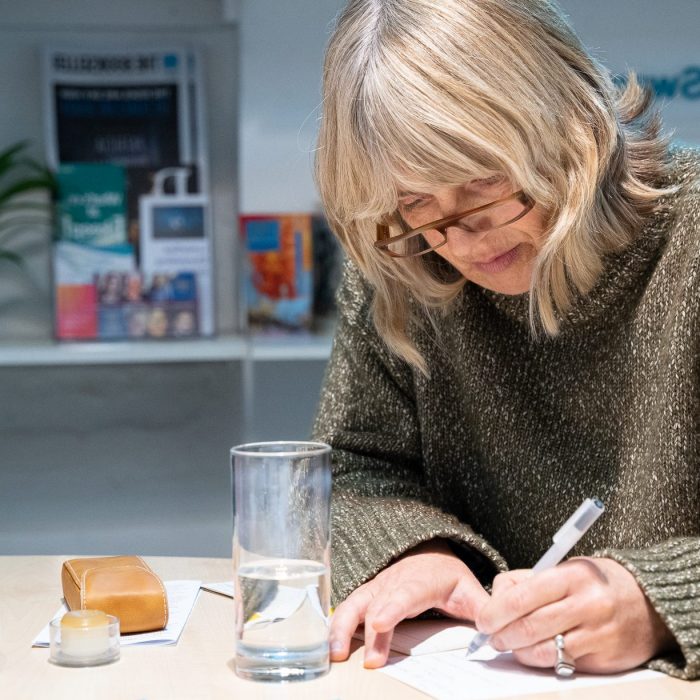 A person writing during a writing workshop. They have brown glasses and shoulder length blonde hair.