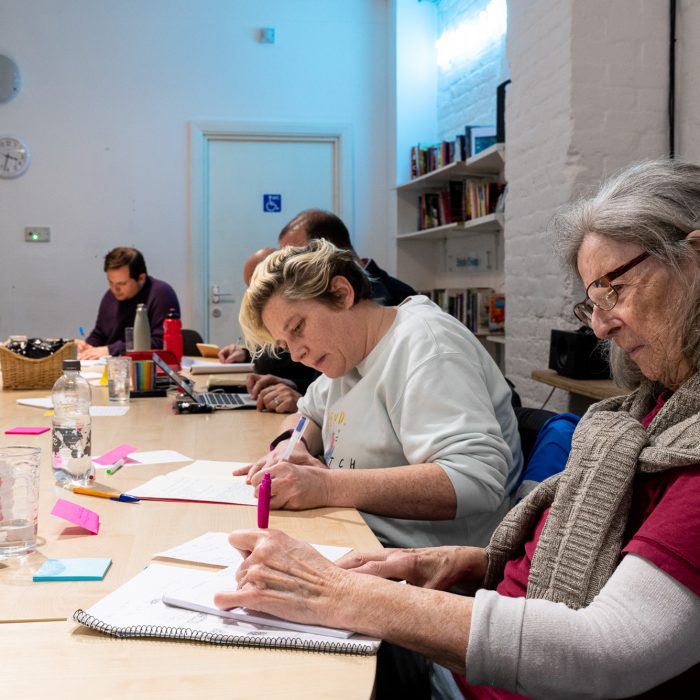 A group of people are sat round a table writing at our writing workshop.